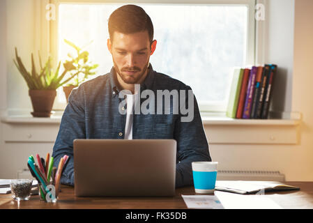 Unternehmer bei einem Laptop Computer tippen arbeiten oder Surfen im Internet mit einem intensiven vertieft Ausdruck Stockfoto