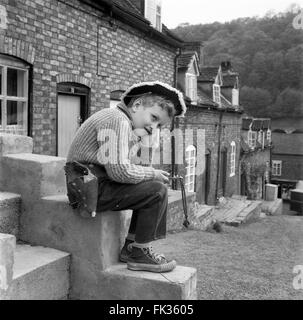 Kleiner Junge, der alleine mit einem Katapult spielt und ein Cowboy-Outfit trägt 1960s Britain UK Street vor den Straßen Stockfoto