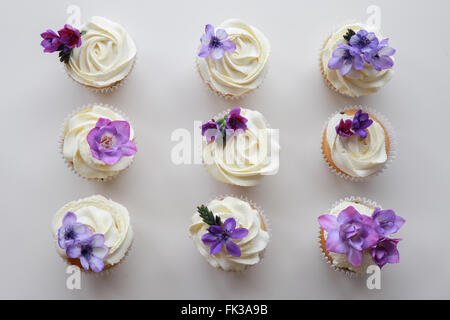Hausgemachte lila Freesie Blumen auf Vanille Cupcakes mit gepeitschter Creme Zuckerguss Stockfoto