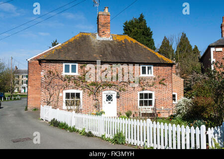 Freistehende gemauerte Doppel - 2-stöckiges Haus mit Glasfront mit Efeu wächst über der Tür. Weißen Zaun und Straße entlang laufen. Blauer Himmel, strahlender Sonnenschein. Stockfoto