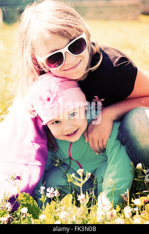 Kleine blonde kaukasische Schwestern umarmen an einem sonnigen Sommertag. Closeup Portrait mit Tonwertkorrektur-Foto-Filter-Effekt Stockfoto