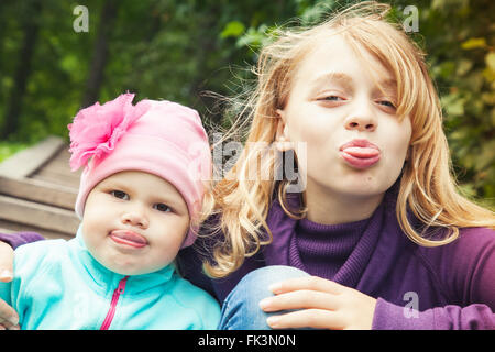 Lustige zeigen wenig blonde kaukasische Schwestern Zungen. Nahaufnahme outdoor Portrait mit Tonwertkorrektur-Foto-Filter-Effekt Stockfoto