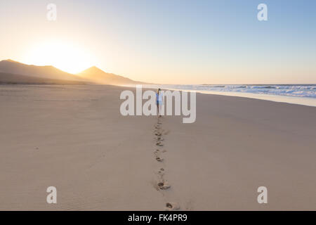 Dame zu Fuß am Sandstrand in Sonnenuntergang Fußabdrücke hinterlassen. Stockfoto