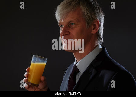 Mann im Anzug lächelnd und Orangensaft trinken Stockfoto