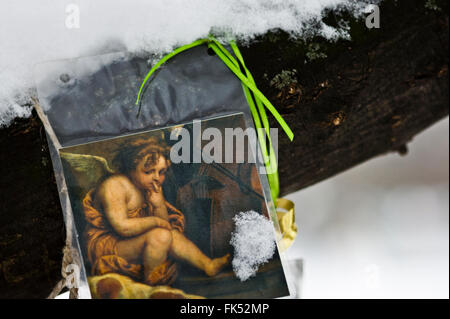 nachdenklicher Engel, Detail der klassischen Malerei zeigt einen Engel, ausgeschnitten und in Kunststoff-Abdeckung gebunden an einen Baum, mit Schnee bedeckt Stockfoto