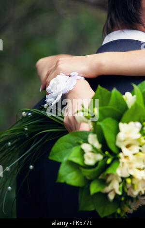 die Braut mit einem weißen Armband und einen grünen Strauß in Händen umfasst stark den Bräutigam Stockfoto