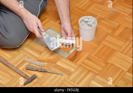 Man setzt Adhäsiv-Paste auf Stücke von Parkett in Wohnung Stockfoto
