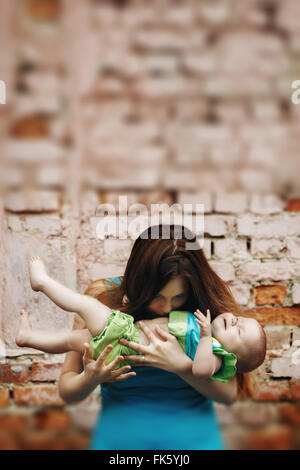Porträt der Liebe junge Mutter halten und küssen ihr Baby gegen Mauer. Selektiven Fokus, Tilt Shift verschwommenen Effekt. Stockfoto