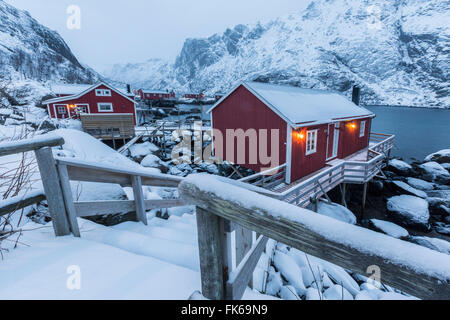 Typische Fischerhäuser Rorbu genannt, in die verschneite Landschaft bei Dämmerung, Nusfjord, Nordland County, Lofoten Inseln, Norwegen Stockfoto