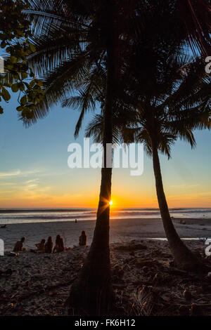 Menschen, die von Palmen bei Sonnenuntergang am Strand von Playa Hermosa, weit südlich der Halbinsel Nicoya, Santa Teresa, Puntarenas, Costa Rica Stockfoto