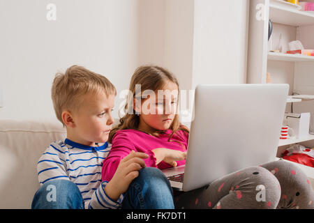 Kinder zu Hause sitzen auf Sofa, spielen mit laptop Stockfoto