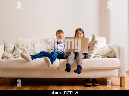 Kinder zu Hause sitzen auf Sofa, spielen mit laptop Stockfoto