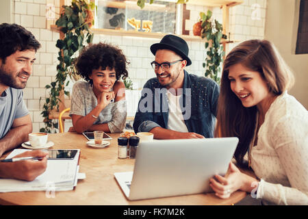 Gruppe von Freunden in einem Café mit einem Laptop unter ihnen hängen. Glückliche junge Menschen sitzen im Restaurant mit laptop