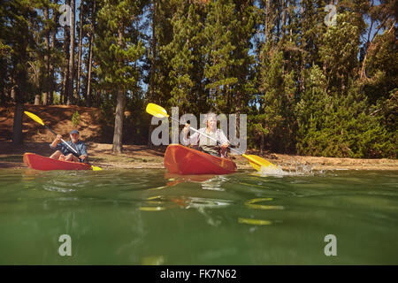 Portrait über ein älteres paar Kanufahren auf einem See bei einem camping-Ausflug. Aktive Senioren Paar in zwei einzelnen Kajaks im See. Stockfoto