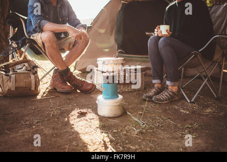 Schuss von reifes Paar sitzen um einen Campingkocher beschnitten. Mann und Frau sitzen im Stuhl außerhalb Zelt auf ihrem Campingplatz. Stockfoto