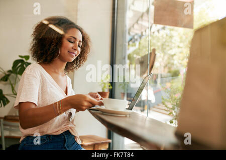 Aufnahme des jungen Afrikanerin in einem Café sitzen und Kaffee trinken. Afrikanische Frau mit Laptop mit Kaffee im Restaurant. Stockfoto