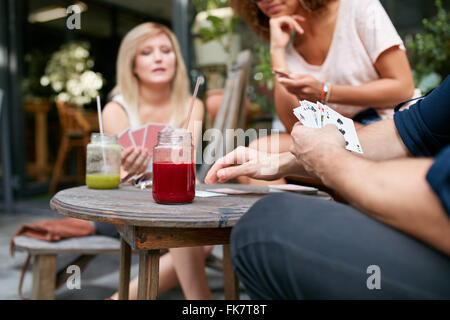 Schuss von jungen Freunden sitzen im Café im freien Spielkarte Spiel beschnitten. Spieler mit den Karten beim Sitzen über die tabl Stockfoto