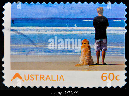 Australien - ca. 2011: Briefmarke gedruckt in Australien lebenden gewidmet australische, zeigt junge Mann mit seinem Hund das Meer zu beobachten Stockfoto