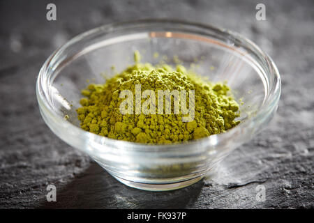 Grünen Matcha-Pulver in eine Glasschüssel auf schwarzen Steinplatte Stockfoto