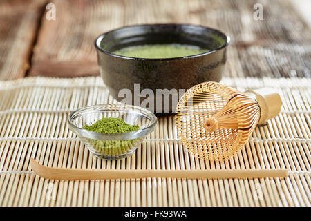 Grünen Matcha Teezubereitung mit Glasschale Schüssel, Schneebesen, Löffel und Tee auf einer Bambusmatte Tabelle Stockfoto