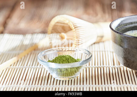 Grünen Matcha Teezubereitung mit Glasschale Schüssel, Schneebesen, Löffel und Tee auf einer Bambusmatte Tabelle Stockfoto
