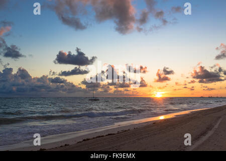 Flauschige Wolken schwebend über turbulente Meerwasser direkt am Sandstrand. Stockfoto