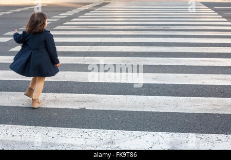 Kleines Mädchen laufen und allein einem Zebrastreifen überqueren. Gefährliches Verhalten Stockfoto