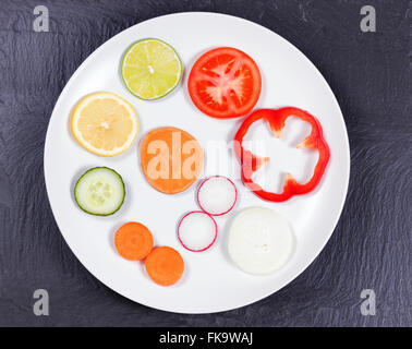 Draufsicht auf verschiedenen geschnittenem Gemüse und Obst in weißer Teller auf schwarzem Schiefer. Stockfoto