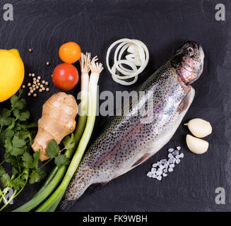 Draufsicht der ganze Fisch mit verschiedenen Kräutern, Gemüse und Gewürzen auf schwarzen Naturzustand. Gesunde Ernährung-Konzept. Stockfoto