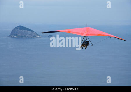 Hängegleiter fliegen über den Strand von Sao Conrado mit Felsformation im Hintergrund Stockfoto