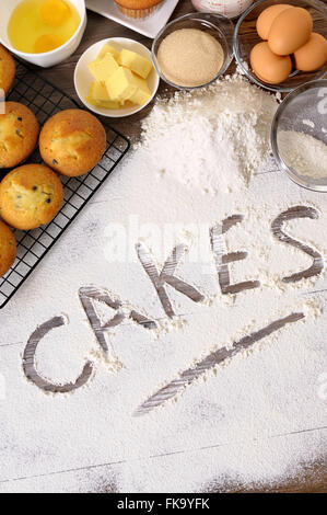 Das Wort Kuchen Mehl auf einem dunklen Holztisch mit frisch gebackenen Muffins und Zutaten geschrieben. Stockfoto