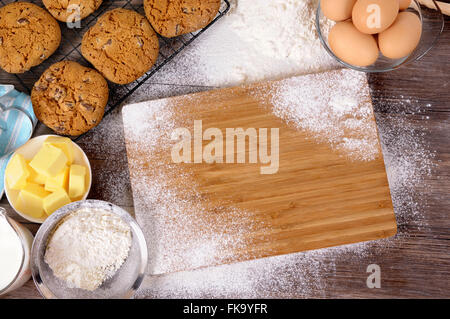 Frisch zubereitete Schokoladenkekse auf einem dunklen Holztisch mit Schneidebrett und Zutaten. Stockfoto