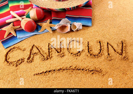 Das Wort Cancun in Sand am mexikanischen Strand mit Sombrero, Strohhut, traditionelle Sarape Decke, Seesterne und Maracas geschrieben. Stockfoto