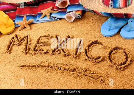 Das Wort Mexiko geschrieben in Sand am mexikanischen Strand mit Sombrero, Strohhut, traditionelle Sarape Decke, Seesterne und Muscheln Stockfoto