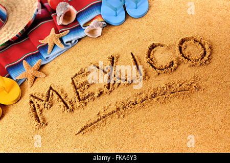 Das Wort Mexiko geschrieben in Sand am mexikanischen Strand, mit Stroh Sombrero-Hut, traditionelle Sarape Decke, Seesterne und Muscheln. Stockfoto