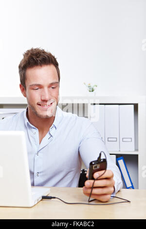 Glücklich College-Student am Schalter Handy mit Laptop über USB aufladen Stockfoto