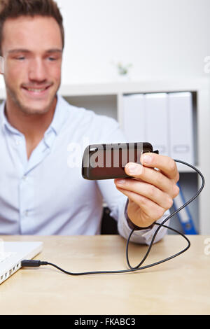 Junger Geschäftsmann übertragen von Bildern vom Handy per USB an Rechner Stockfoto