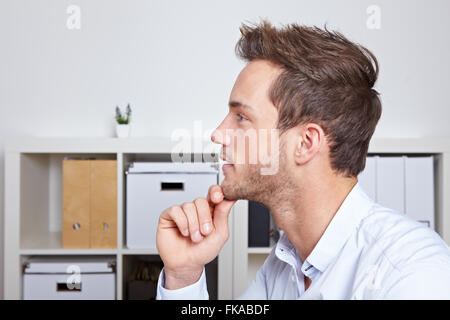 Junger Geschäftsmann in der Profilansicht mit Hand am Kinn im Büro Stockfoto