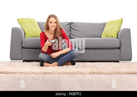 Junge Brünette Frau vor einem grauen Sofa sitzen und Fernsehen isoliert auf weißem Hintergrund Stockfoto