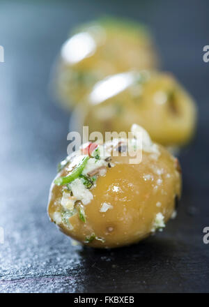 Portion eingelegte grüne Oliven mit Knoblauch und frischen Kräutern Stockfoto