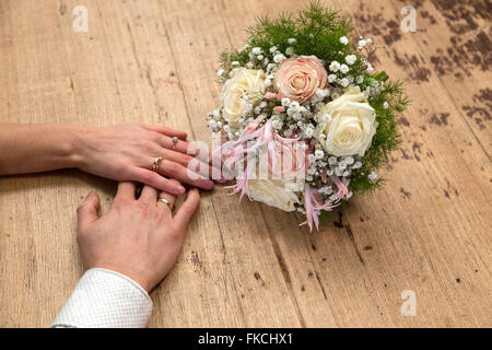 Hände der Braut und des Bräutigams mit Ehering auf Holztisch mit Rosenstrauß Stockfoto