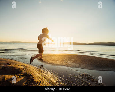 Kleiner Junge (4-5) an sonnigen Tag über Wasser springen Stockfoto