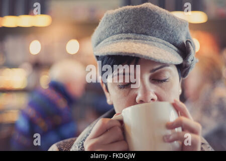 Frauen trinken schmackhafte warme Getränke tragen eines Winter" hat mit ihren Augen in der Kontemplation Stimmung herunterfahren Stockfoto