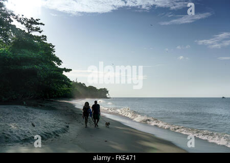 Paar mit Hund zu Fuß am Sandstrand, Trinidad, Trinidad und Tobago Stockfoto