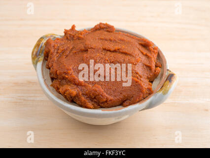 Seitenansicht einer kleinen Schüssel gefüllt mit roter Curry-Paste auf einer hölzernen Tischplatte. Stockfoto