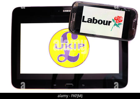 Ein Tablet mit dem UKIP-Logo drauf und ein Smartphone mit dem Labour-Logo drauf vor einem weißen Hintergrund. Stockfoto