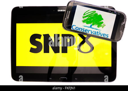 Ein Tablet mit dem SNP-Logo drauf und ein Smartphone mit der konservativen Partei-Logo drauf vor einem weißen Hintergrund. Stockfoto