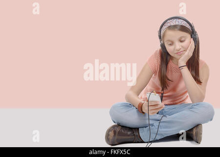 ein pre-teen Mädchen Musikhören mit seinem Smartphone, sitzt im Schneidersitz Stockfoto