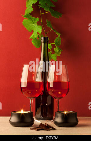 Flasche Rotwein mit zwei Gläser, Kerzen und Pralinen auf rotem Hintergrund und Marmor kitchentop Stockfoto