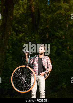 Die blue - eyed hübscher junger Mann gekleidet casual Bike auf der Schulter und wieder grünen Wald Stockfoto